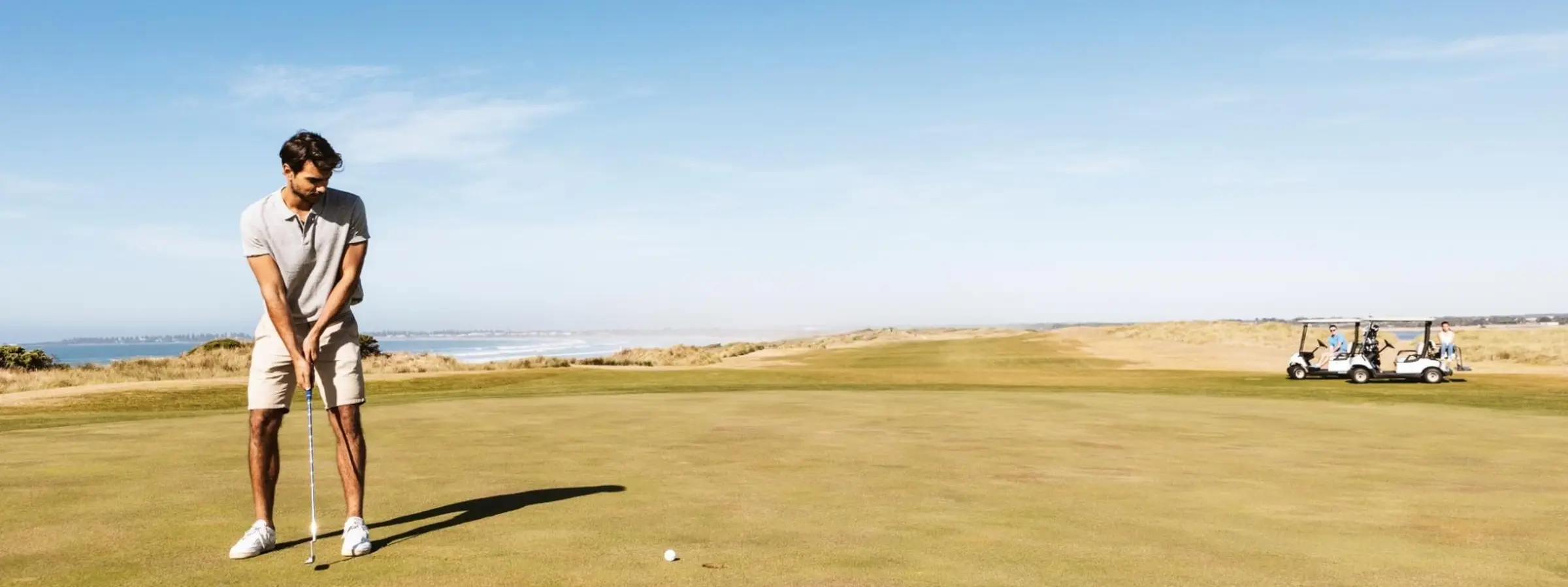Golfer lining up a putt on a coastal golf course with ocean views in the background.