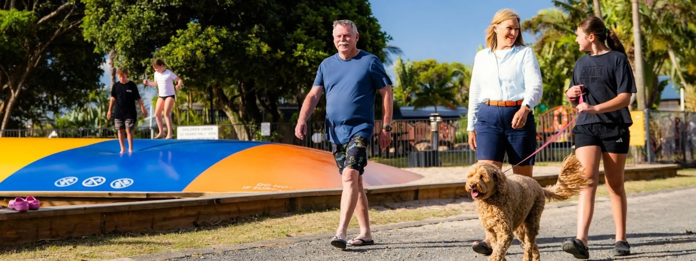 Guests walking their dog at a pet-friendly holiday park, with caravan and camping sites nearby.