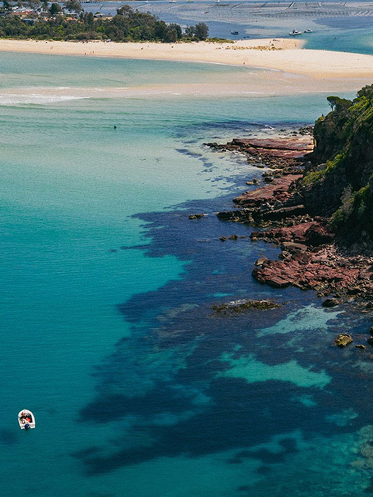 Aerial view of Bar Beach in Merimbula, showcasing turquoise waters, rocky coastline and surrounding bushland on the NSW Sapphire Coast.