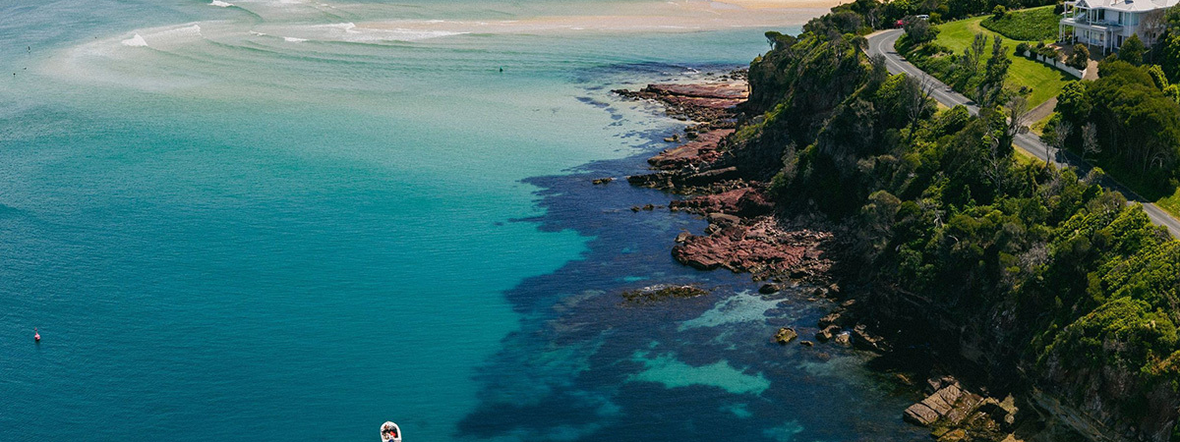 Aerial view of Bar Beach in Merimbula, showcasing turquoise waters, rocky coastline and surrounding bushland on the NSW Sapphire Coast.