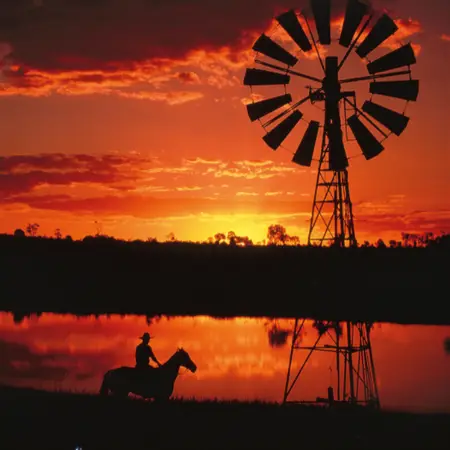 A sunset over a dam in Longreach, with the silhouette of a person on horseback and a windmill