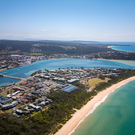Aerial view of Black Dolphin Holiday Park and Motel in Merimbula, showing the motel buildings, landscaped grounds and nearby Boggy Creek, with its turquoise waters and boat ramp on the NSW Sapphire Coast.