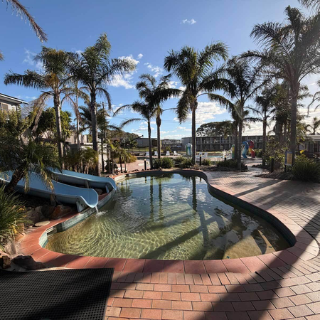 Swimming pool with waterslides surrounded by palm trees and tropical gardens at Black Dolphin Holiday Park in Merimbula, NSW.