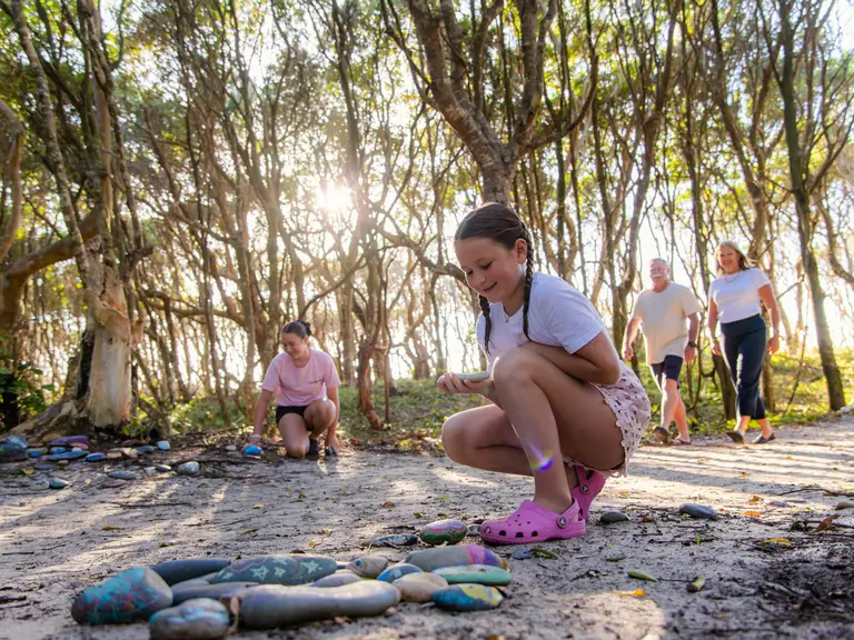 Young girl discovering colourful hand-painted rocks along the walking trail from BIG4 Manning Point Holiday Park to the beach.