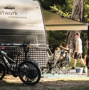 Guests relaxing on a powered caravan site surrounded by nature in Warburton.