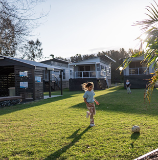 Child playing on the grassy grounds beside accommodation at Barlings Beach Holiday Park