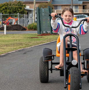 Merimbula holiday park: child riding a pedal go-kart along a paved park pathway