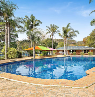 Outdoor swimming pool surrounded by palm trees at Barlings Beach Holiday Park on the NSW South Coast