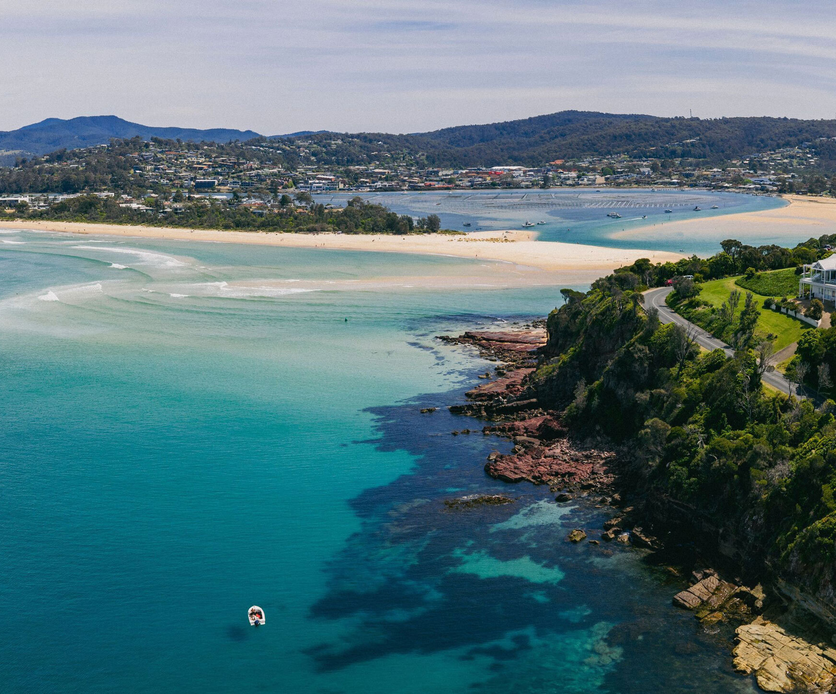 Aerial view of Bar Beach in Merimbula, showing turquoise waters, rocky coastline and views across Merimbula Lake on the NSW Sapphire Coast.