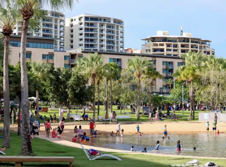 An exciting image of the DWAquaPark at the Darwin Waterfront in Northern Territory, Australia. The photo shows people enjoying the inflatable water playground, which is located in a man-made lagoon. This attraction is a popular spot for families and groups of friends to have fun while camping or staying at a nearby caravan park or holiday park.